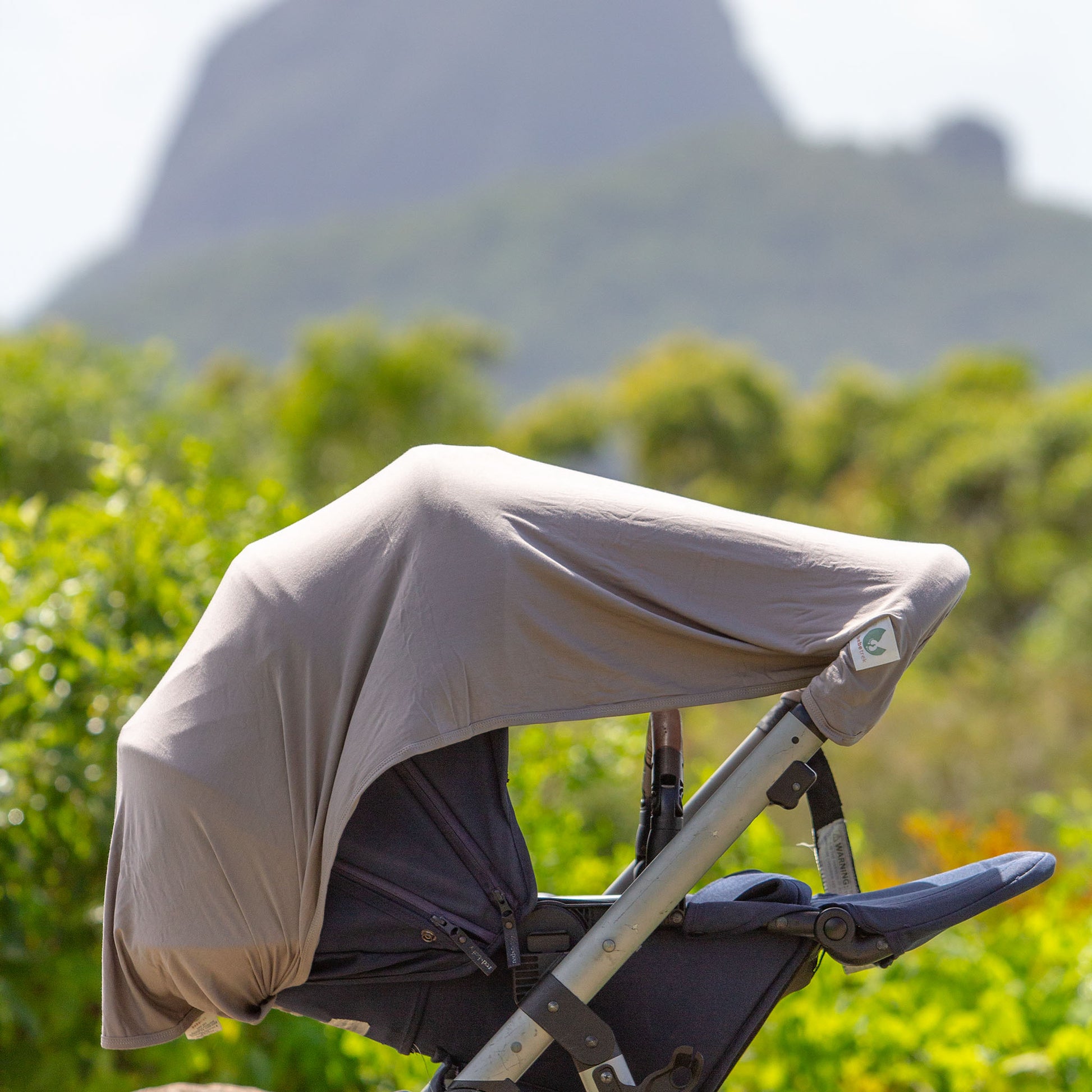 The Bebe Trek Multifunctional magnetic sun cover in earth grey being used a pram shade cover.